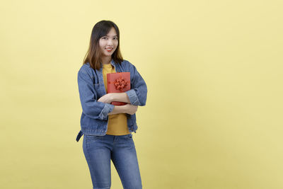 Portrait of young woman standing against yellow background