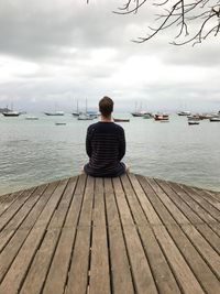 Rear view of woman sitting on jetty against sea