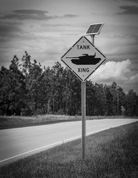 Road sign by trees on field against sky