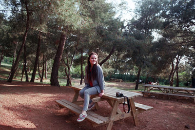 Full length of young woman sitting on picnic table at park