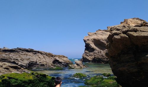 Rock formations by sea against clear blue sky