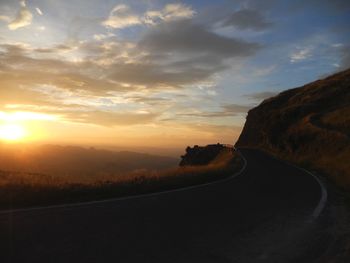 Mountain road against cloudy sky at sunset