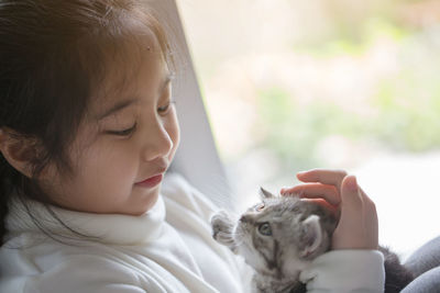 Girl playing with scottish fold cat while sitting by window at home