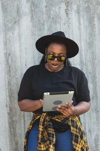 Young woman using mobile phone while standing against wall