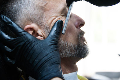 Cropped hands of barber trimming beard of man at salon