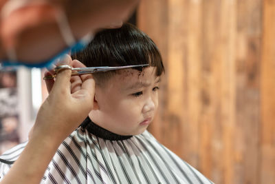 Cropped hand of barber cutting hair of boy