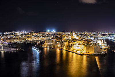 Illuminated buildings by river against sky at night