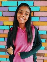 Portrait of smiling teenage girl standing against colorful wall