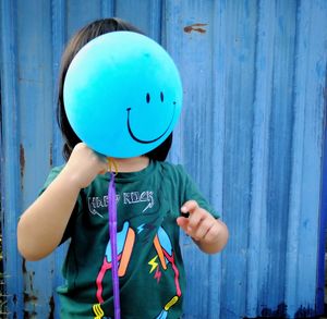 Girl holding balloon while standing against corrugated iron 