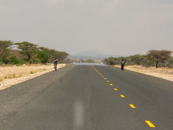 Rear view of people walking on road against clear sky