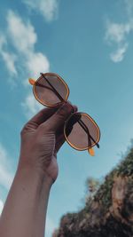 Low angle view of hand holding sunglasses against sky