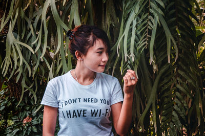 Young woman looking away while standing against plants