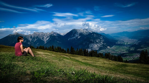 Woman sitting on grassy hill against mountains