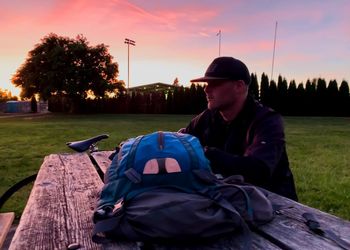 Man sitting on field against sky at sunset