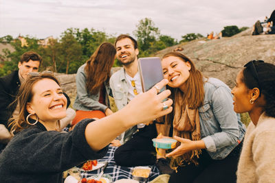 Smiling woman taking selfie with friends during picnic