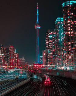 Train on railroad track against illuminated buildings in city at night