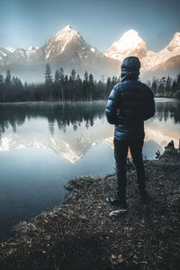 Man standing by lake against mountain during winter