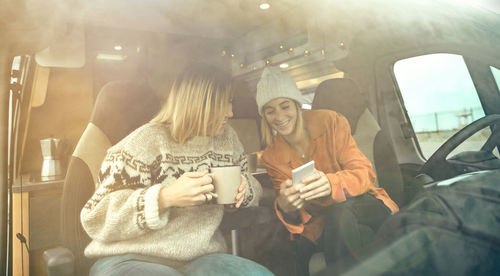 Women laughing looking mobile sitting in the front seat of a camper van