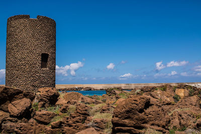 Tower by rocks against blue sky at castelsardo