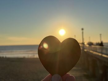 Person holding heart shape against sky during sunset