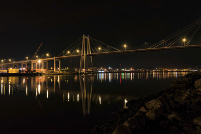 Illuminated bridge over river against sky at night