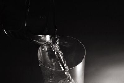 Close-up of glass pouring water against black background