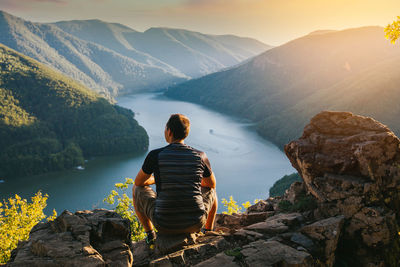 Rear view of man sitting on rock looking at mountains