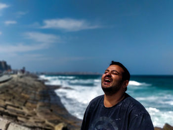 Man laughing while standing against sea and sky