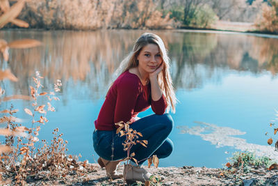 Portrait of young woman crouching at lakeshore