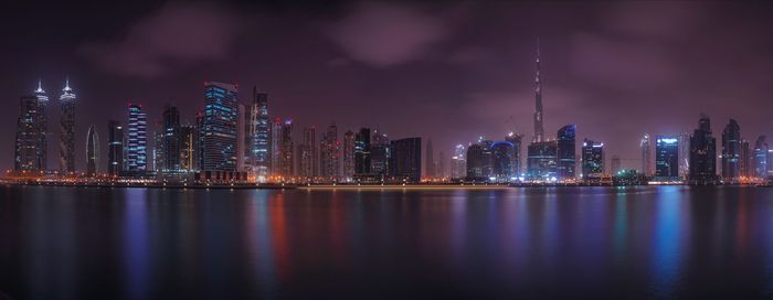 Panoramic view of illuminated city by marina at night