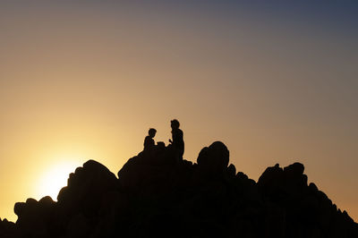 Silhouette people on rock against sky during sunset