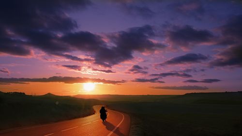 Silhouette woman on road against sky during sunset