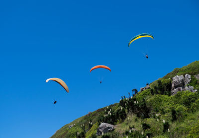 Low angle view of paragliding against clear blue sky