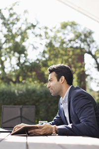 Side view of young businessman with laptop at outdoor restaurant
