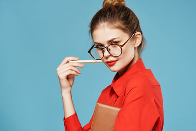 Portrait of woman holding eyeglasses against blue background