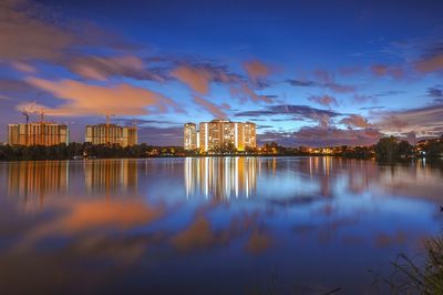 Illuminated buildings by lake against sky at night