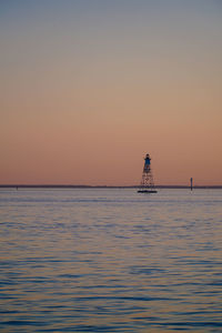 Silhouette tower on sea against clear sky during sunset