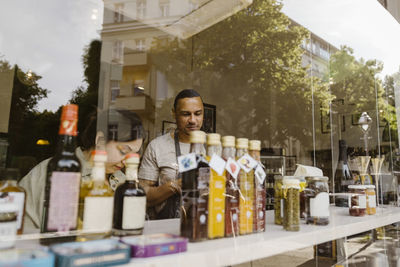 Male and female owners arranging merchandise on shelf seen through glass window