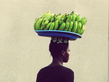 Rear view of man carrying bananas on head against wall