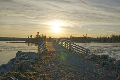 Pier over river against sky during sunset