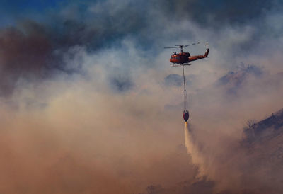 Low angle view of helicopter spraying water against cloudy sky