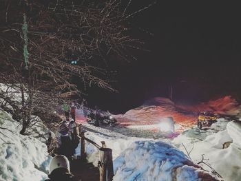 People on snow covered land against mountain at night