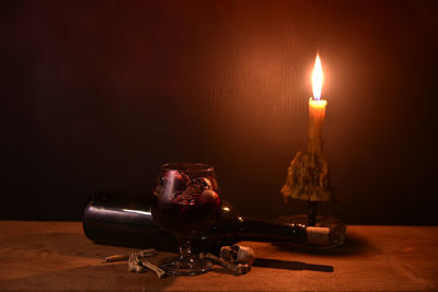 Close-up of lit candle by drink in glass and bottle with bones on table