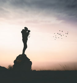 Silhouette woman photographing birds flying against sky during sunset