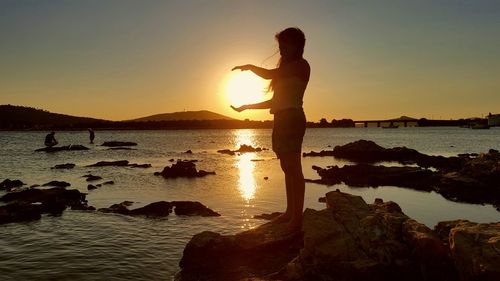 Optical illusion of woman holding sun while standing at beach during sunset
