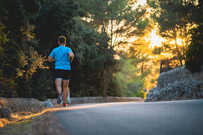 Rear view of young man jogging on road