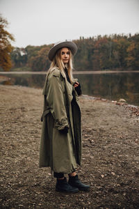 Portrait of woman wearing hat standing by lake against sky