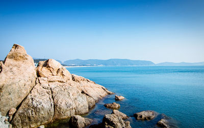 Rocks by sea against clear blue sky