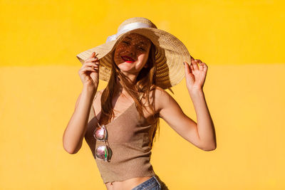 Woman wearing hat standing against yellow background