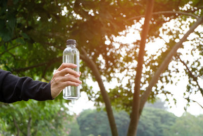 Man holding glass bottle against trees